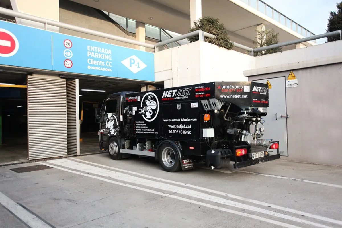 
La imagen muestra un camión de desatasco de tuberías de la empresa NetJet ingresando a un estacionamiento subterráneo, probablemente para realizar servicios de limpieza o mantenimiento en el sistema de drenaje. El vehículo está equipado con maquinaria especializada para desatascar y limpiar tuberías, como mangueras a presión y otros equipos. 