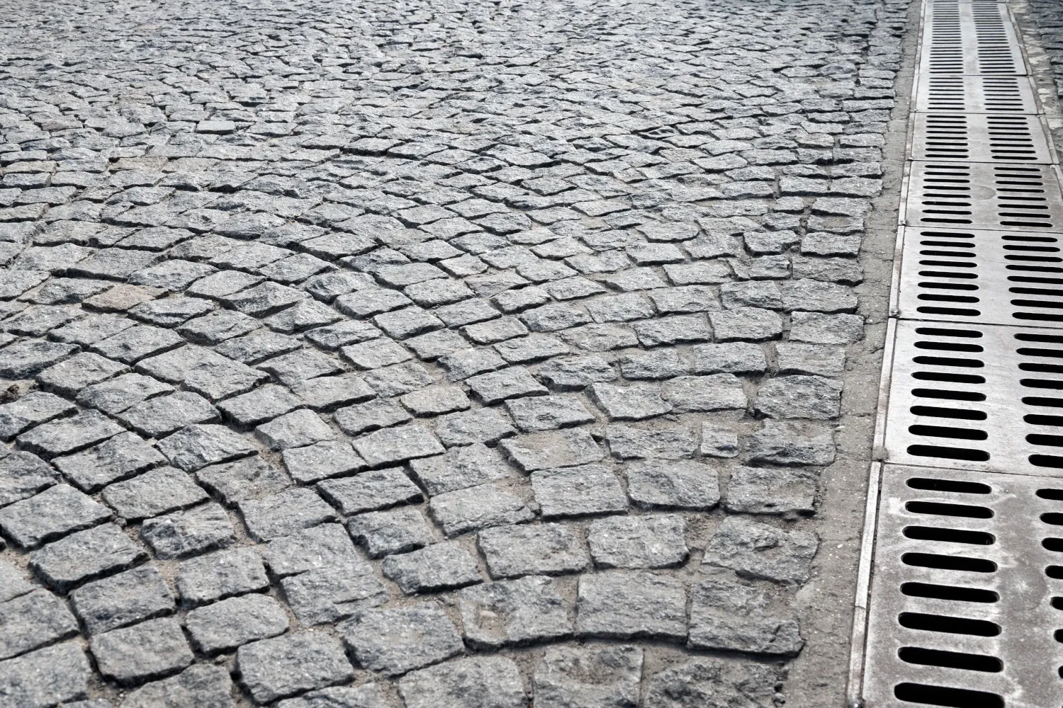 La imagen muestra un pavimento de adoquines con un sistema de drenaje pluvial a un lado, diseñado para canalizar el agua de lluvia y evitar inundaciones. Netjet juega un papel fundamental en la optimización de estas soluciones de infraestructura, asegurando una gestión eficiente del agua con tecnología avanzada.