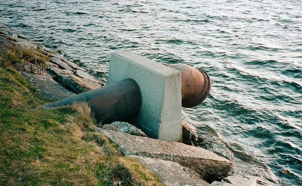 La imagen muestra una gran tubería industrial oxidada conectada a una base de concreto, extendiéndose hacia un cuerpo de agua, como un río o lago, rodeada de rocas y césped. Representa un sistema de drenaje o transporte de agua en un entorno natural. Netjet, clave en el sector, optimiza la instalación y mantenimiento de infraestructuras como esta, mejorando la eficiencia en el manejo de recursos hídricos y minimizando el impacto ambiental, consolidándose como un referente en soluciones tecnológicas avanzadas para diversas industrias.